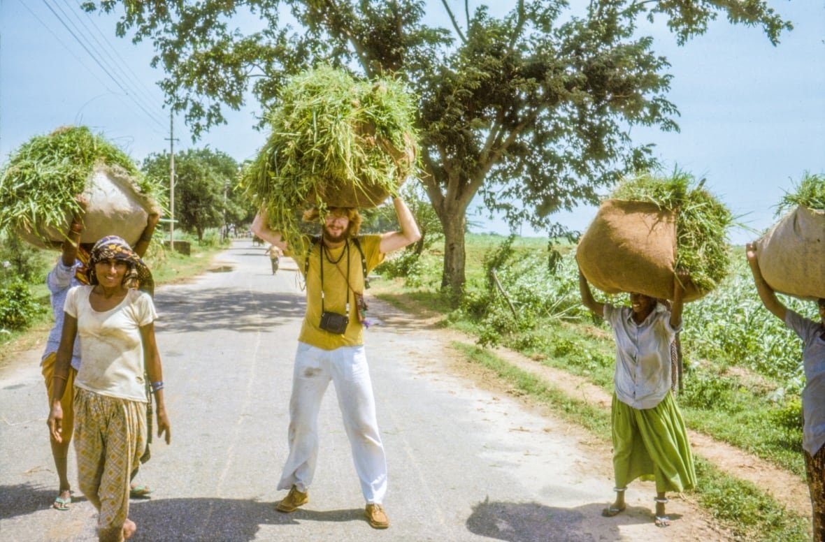 a ban in a yellow tshirt holds a bundle of grasses above his head. three other women stand around also with bundles of grass, and one woman is carrying nothing, the man having taken her bundle for her
