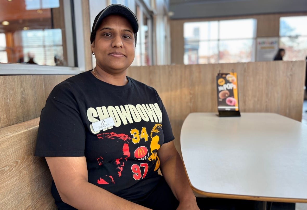 Woman in McDonald's restaurant uniform and ball cap wipes down a white table.