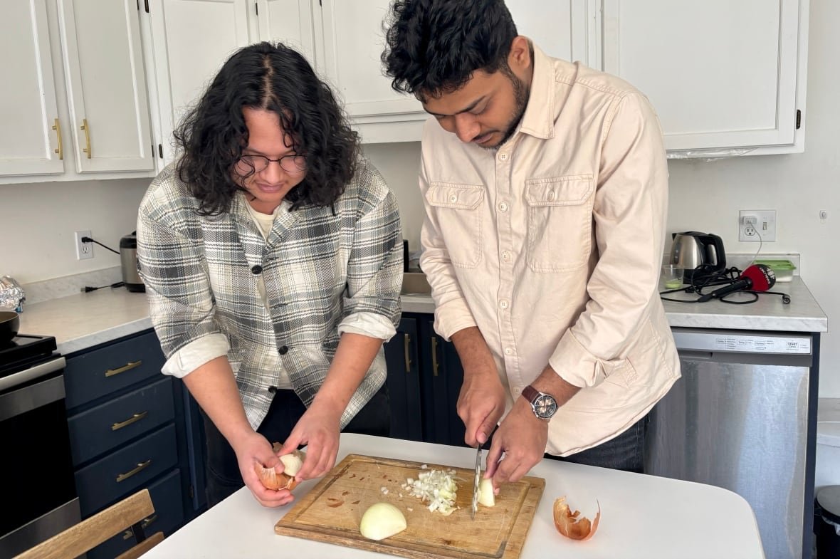 Two young men cut onions in a kitchen.