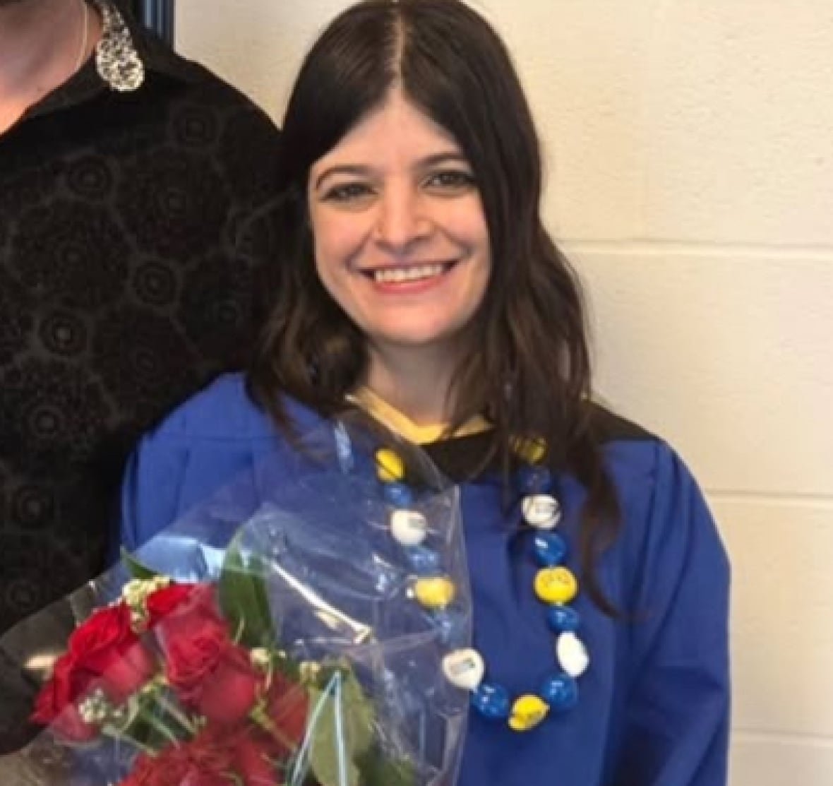 shalini-singh-1 woman stands in a graduation gown holding bouquet of flowers