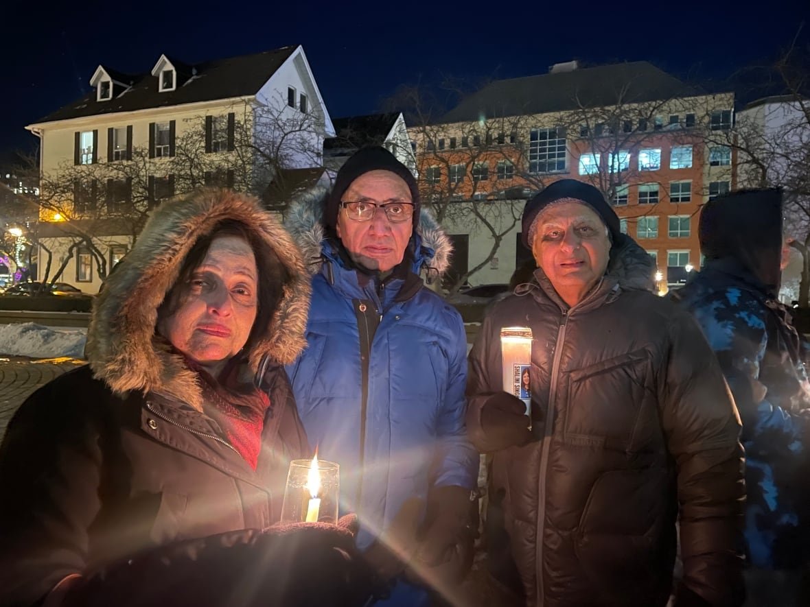 shalini-singh-vigil Three people stand outside, two holding candles.