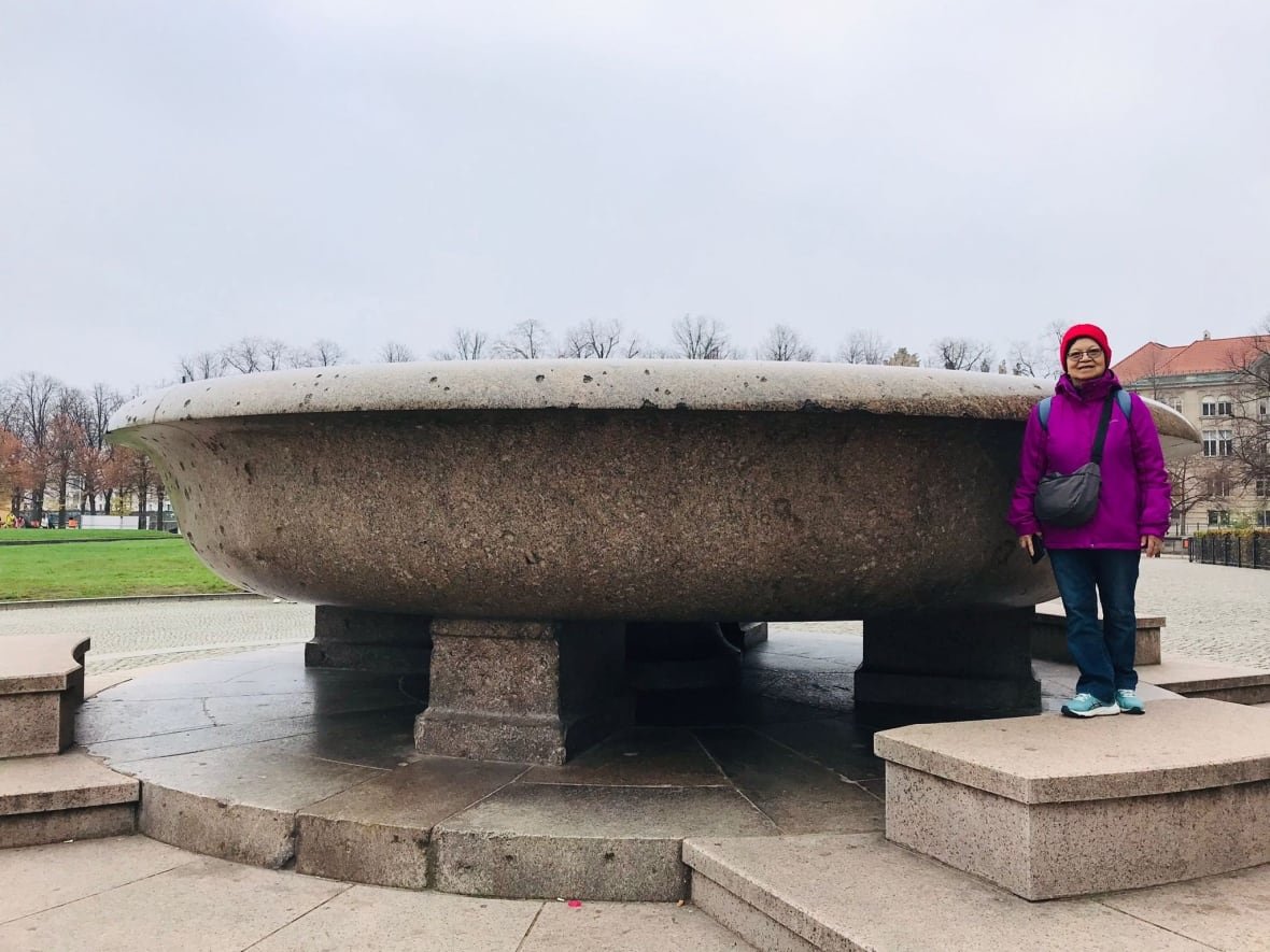 Woman in fuchsia jacket standing beside monument, smiling.