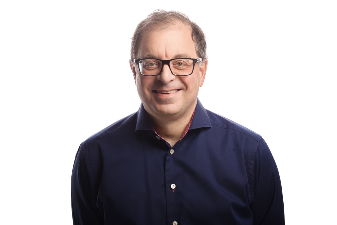 steven-cooper-lawyer Man in a dark blue shirt and white background smiling at the camera.