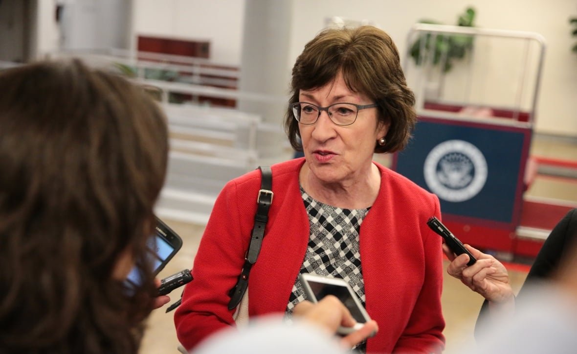 A woman in a red jacket speaks to reporters