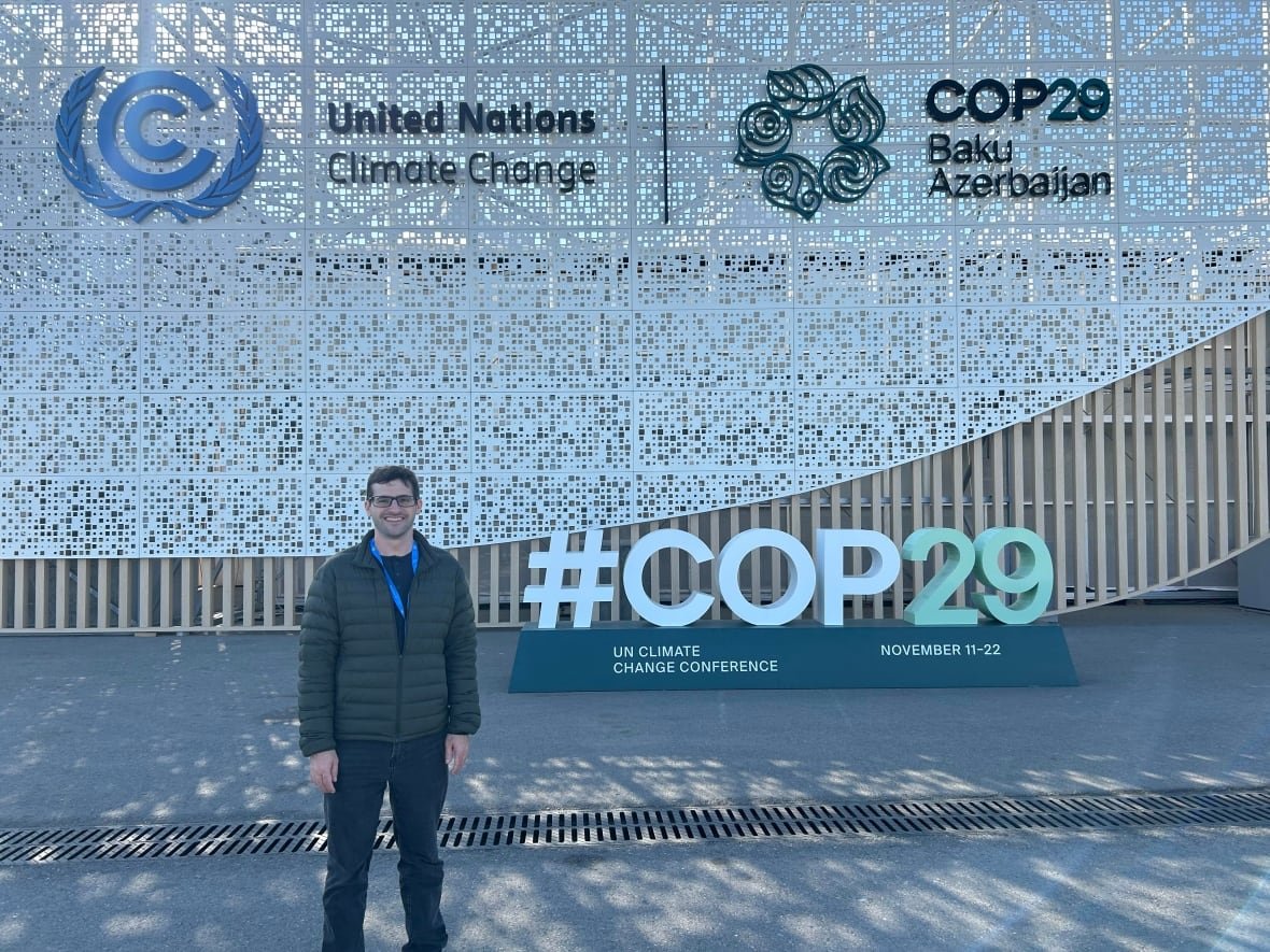 tom-di-liberto Man stands in front of sign reading 'COP29'