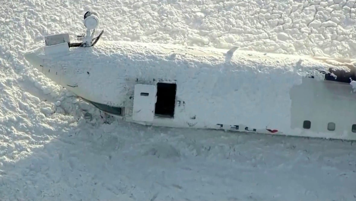 toronto-delta-crash A snow covered airplane lays on a runway overturned.