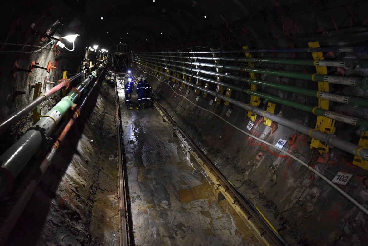uranium-mine-20150923-1 People walk in a dark tunnel lined with pipes underground in a uranium mine.