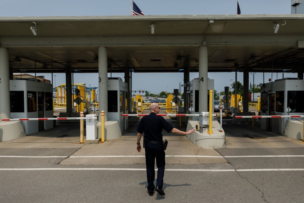 A customs officer singals with his hand as he walks toward a booth at a border crossing.