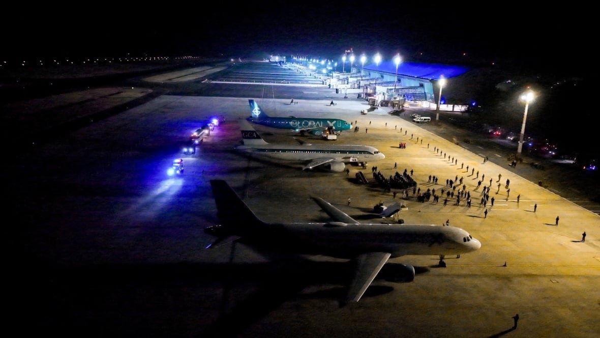 usa-trump-migration-el-salvador-1 An aerial view shows people gathered on a tarmac around parked airplanes.