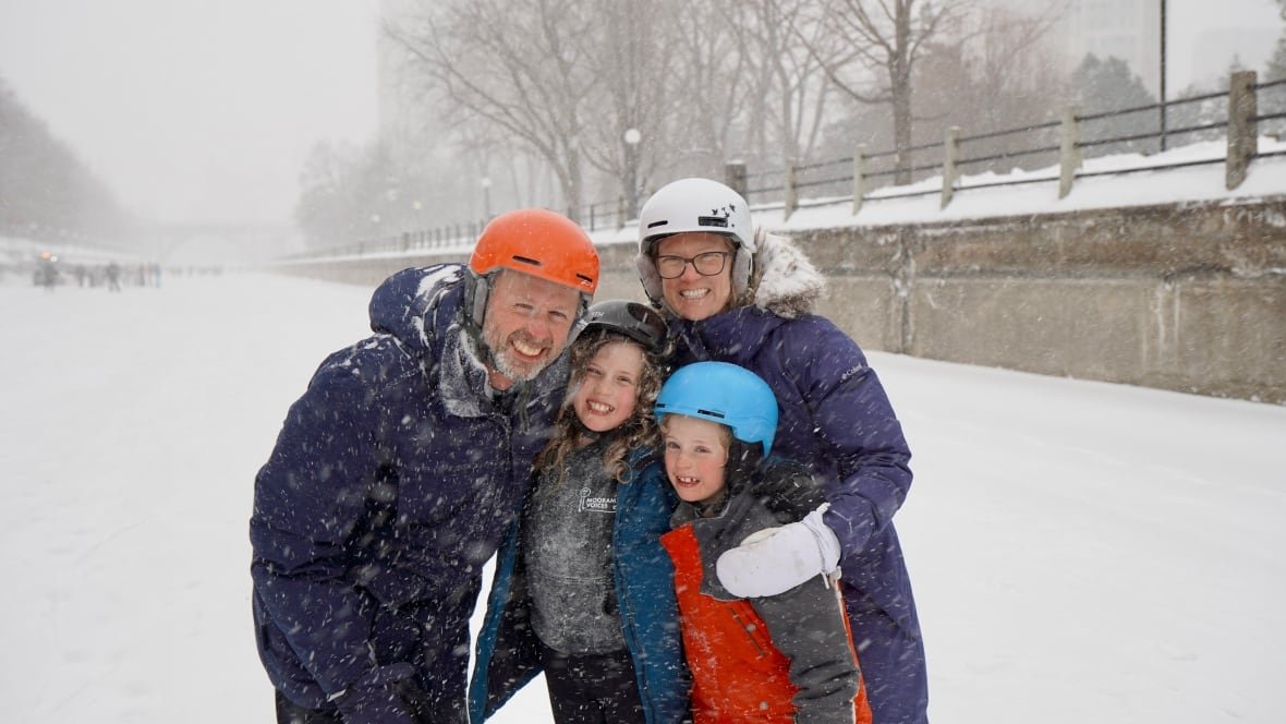 van-den-bos-fam Two parents and two kids smile for a photo on a snowy rideau canal skateway.
