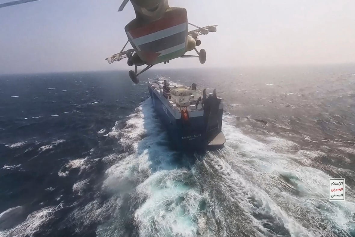 yemen-houthi-red-sea-ship-attacks The view of a helicopter, from below, as it flies toward a merchant vessel on the sea.