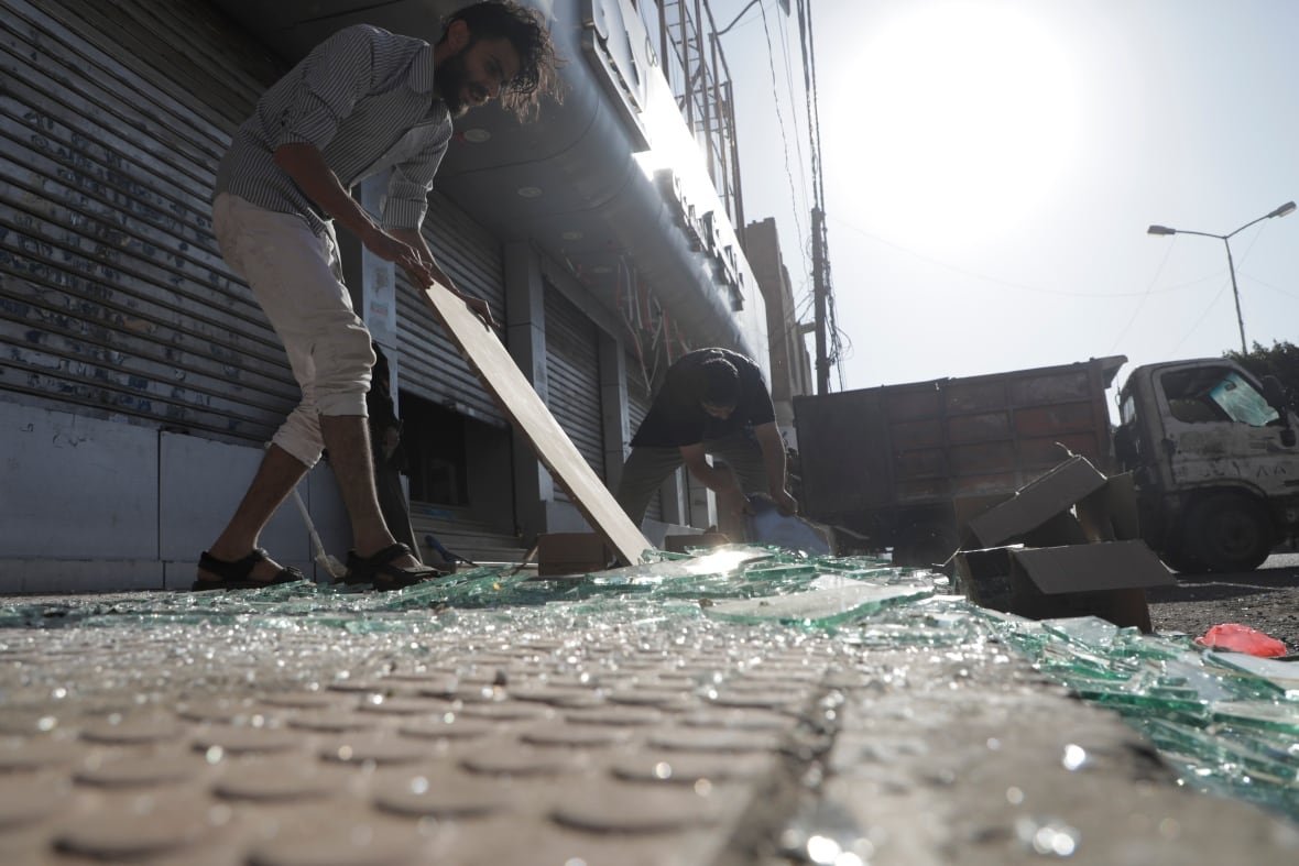 People clean up broken glass on a sidewalk.