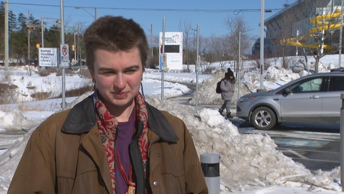 yvren-mestres-wyenberg A person with short hair and piercings standing in front of a parking lot with snow.