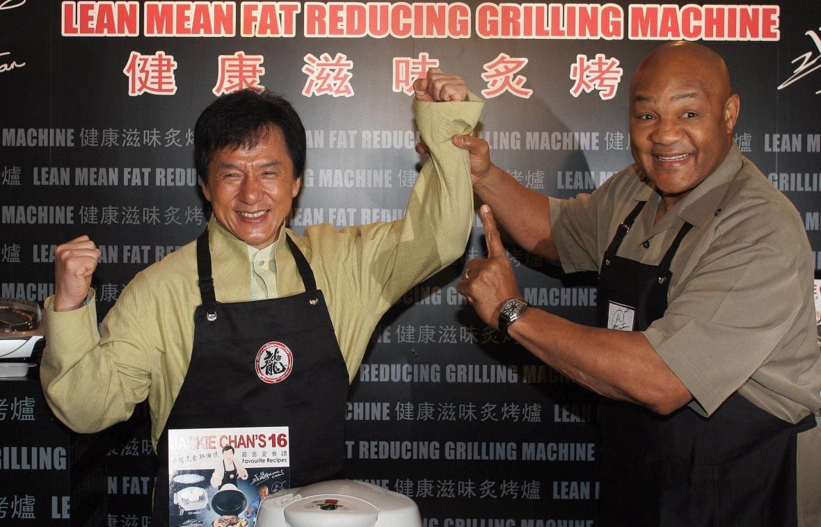 An African American and an Asian hold each other's arms up while wearing an apron.