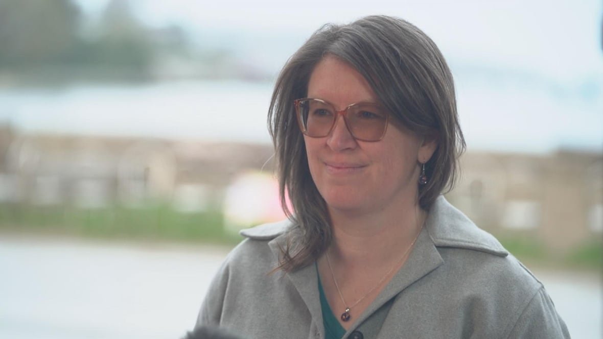 alyssa-gehman A woman wearing sunglasses and a grey jacket smiles.