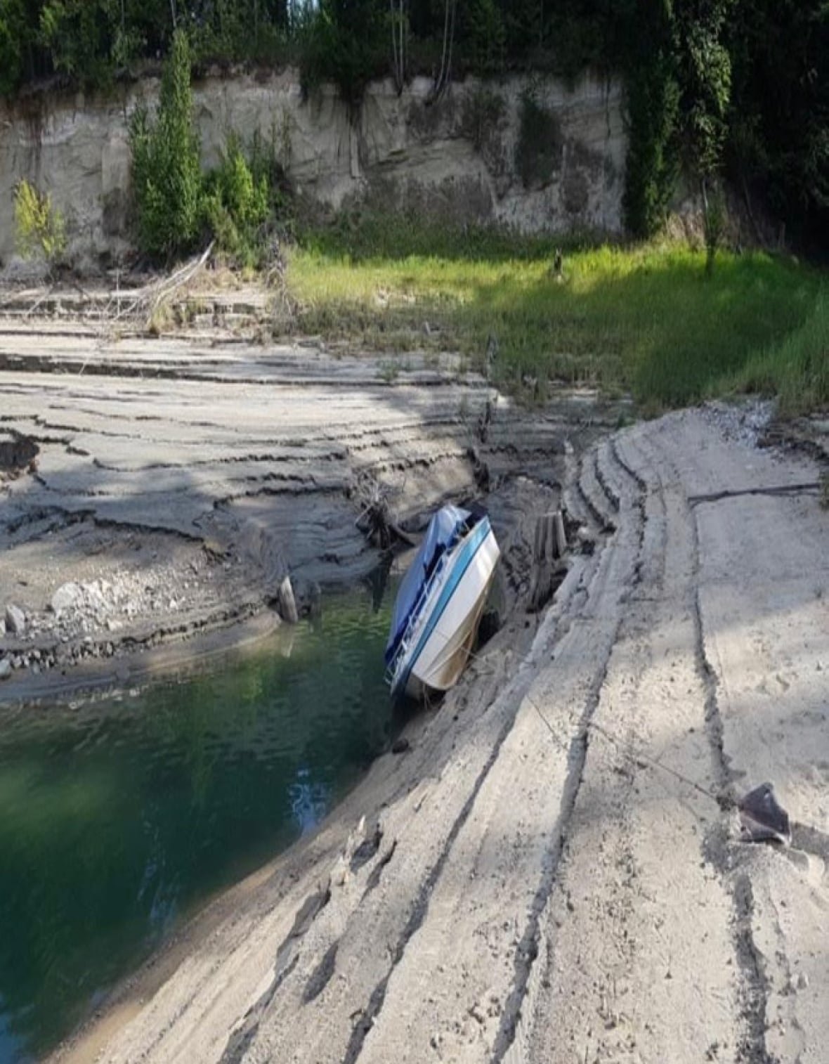 arrow-lakes-water-levels A boat hangs precariously on the side of a lake bottom that has been dry.