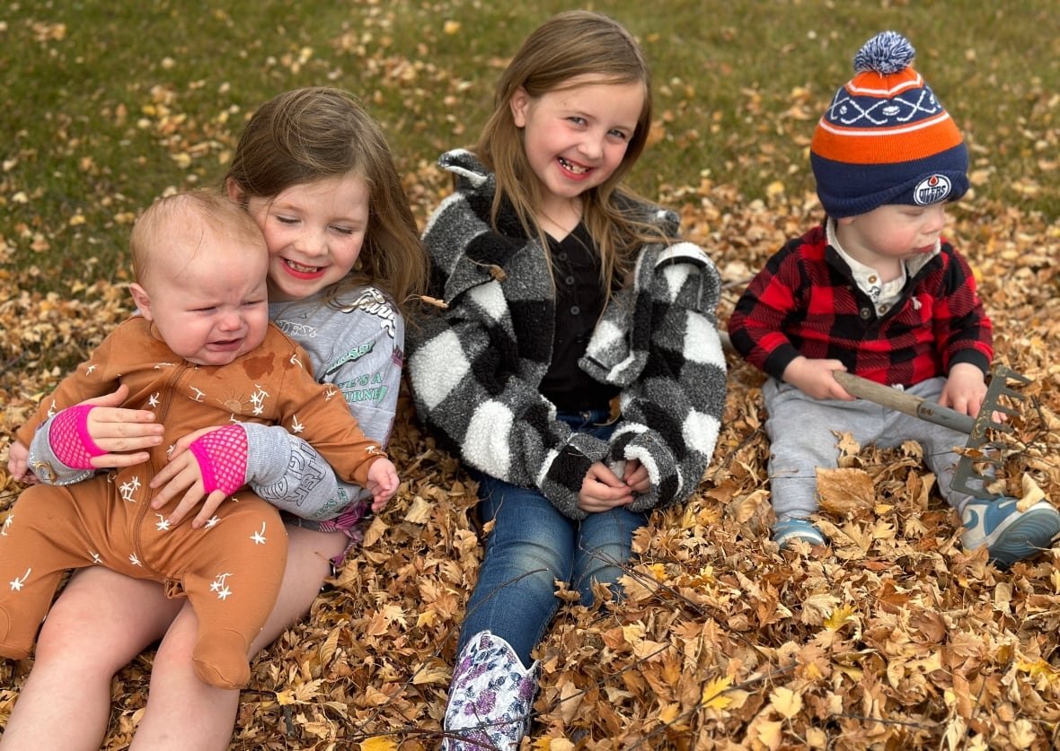 childcare-fees-in-olds-alberta Two girls and two young boys, all siblings, play in a pile of leaves.