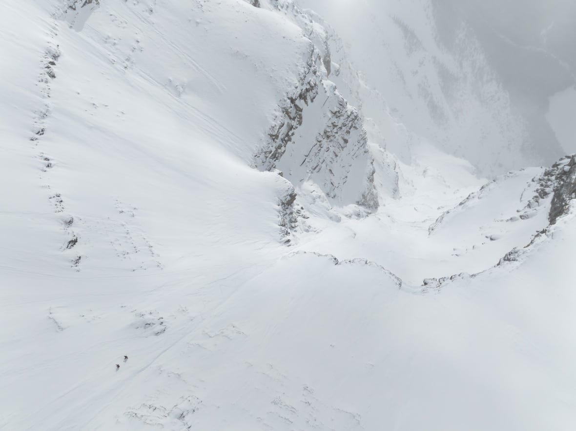 christina-lusti-lustenberger-guillaume-pierrel-ascend-mount-robson A wide aerial shot of a snowy slope with two tiny people traversing it.