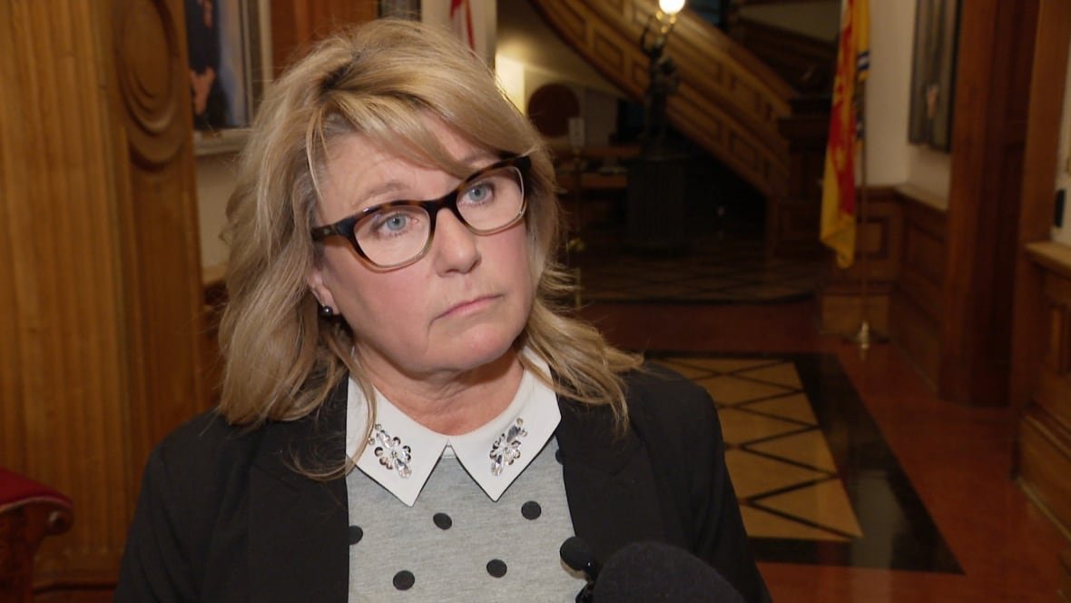 cindy-miles-minister-of-social-development An unsmiling woman wearing a polka-dotted shirt with a bejeweled collar. She has blond shoulder-length hair and is wearing black glasses.