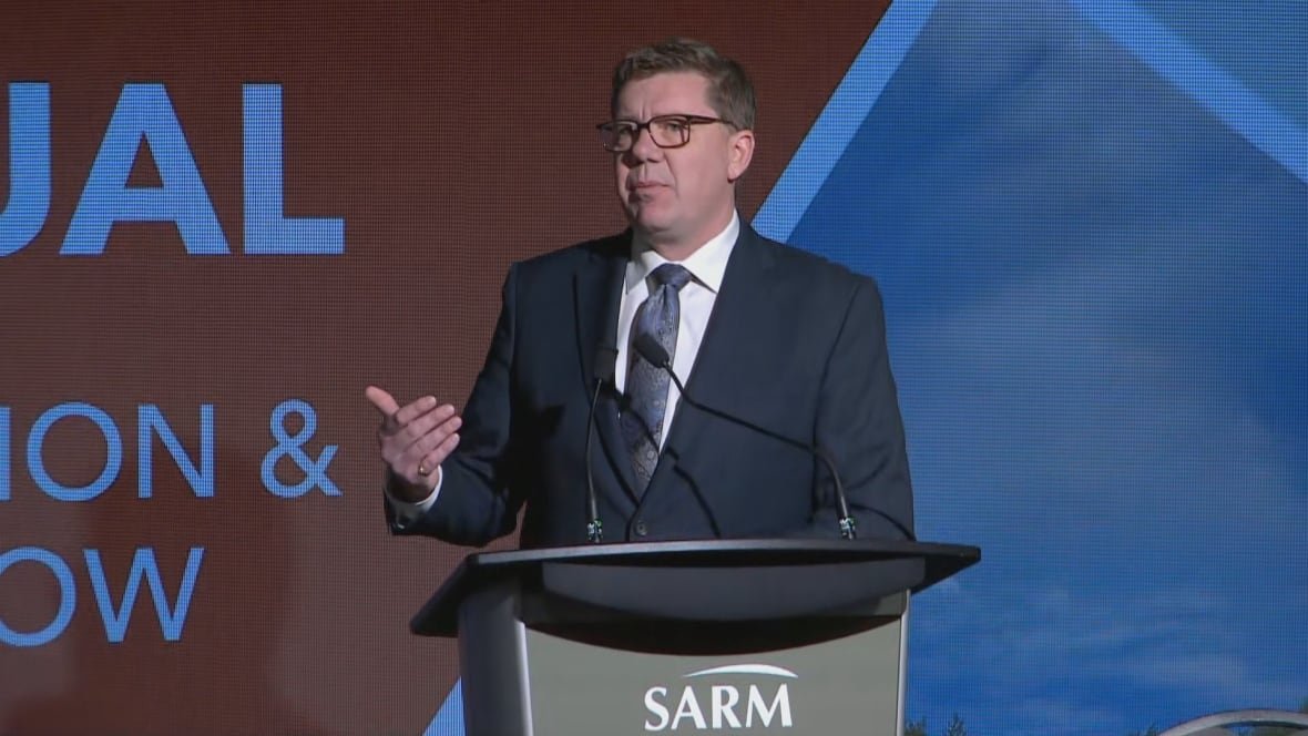 colleen A man with short brown hair and glasses stands behind a podium. He is wearing a blue suit and tie.