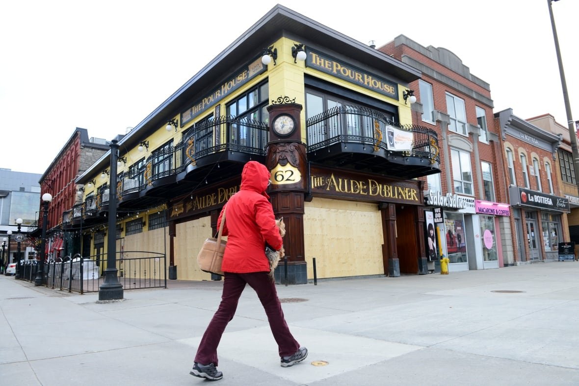 covid-19-byward-market-closed-businesses-ottawa A woman in a coat walks by a boarded up restaurant