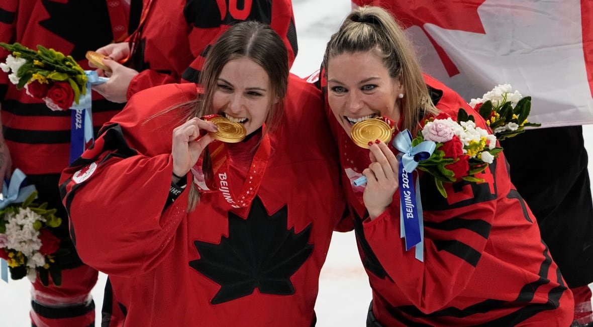 emerance-maschmeyer-and-natalie-spooner Two female Canadian hockey players, wearing red and black Team Canada jerseys, pose with gold medals.