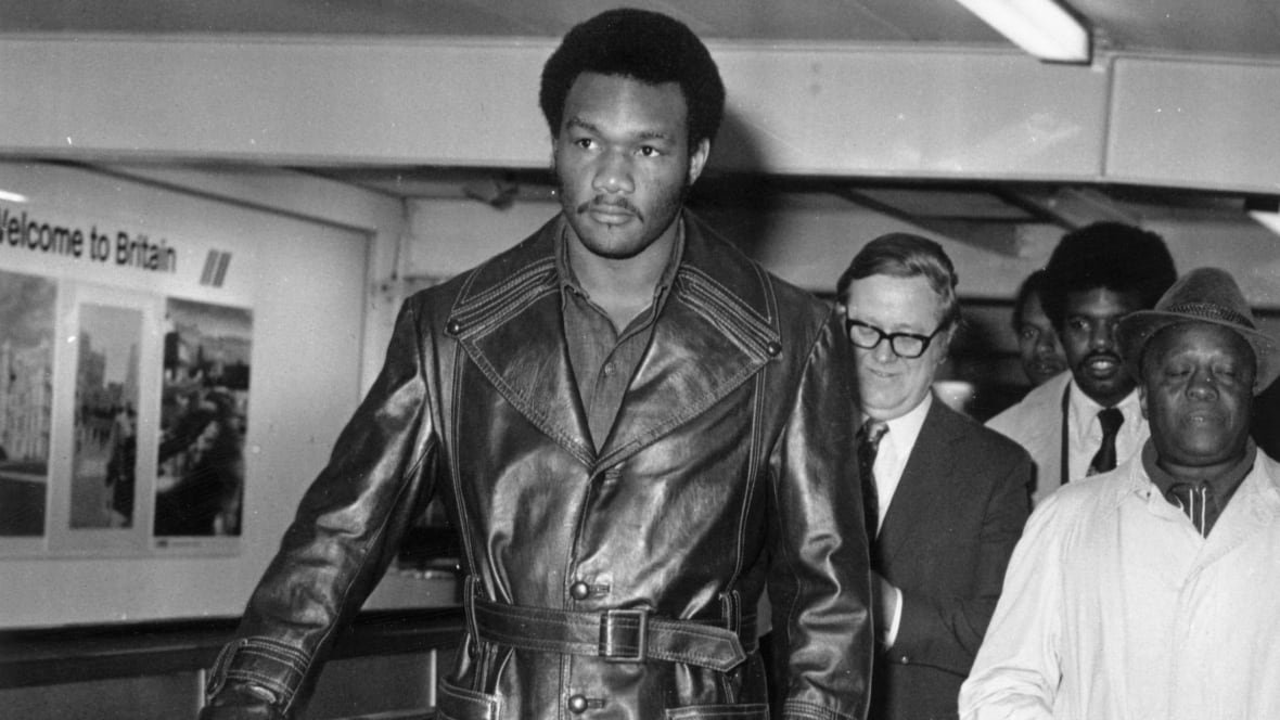 A dark complected man is shown walking in a leather coat in a black and white photograph that appears to be decades old.