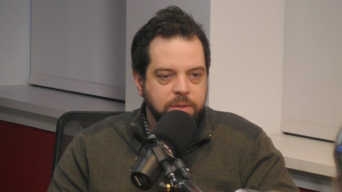 james-ponting A man with brown hair and a beard speaking into a microphone