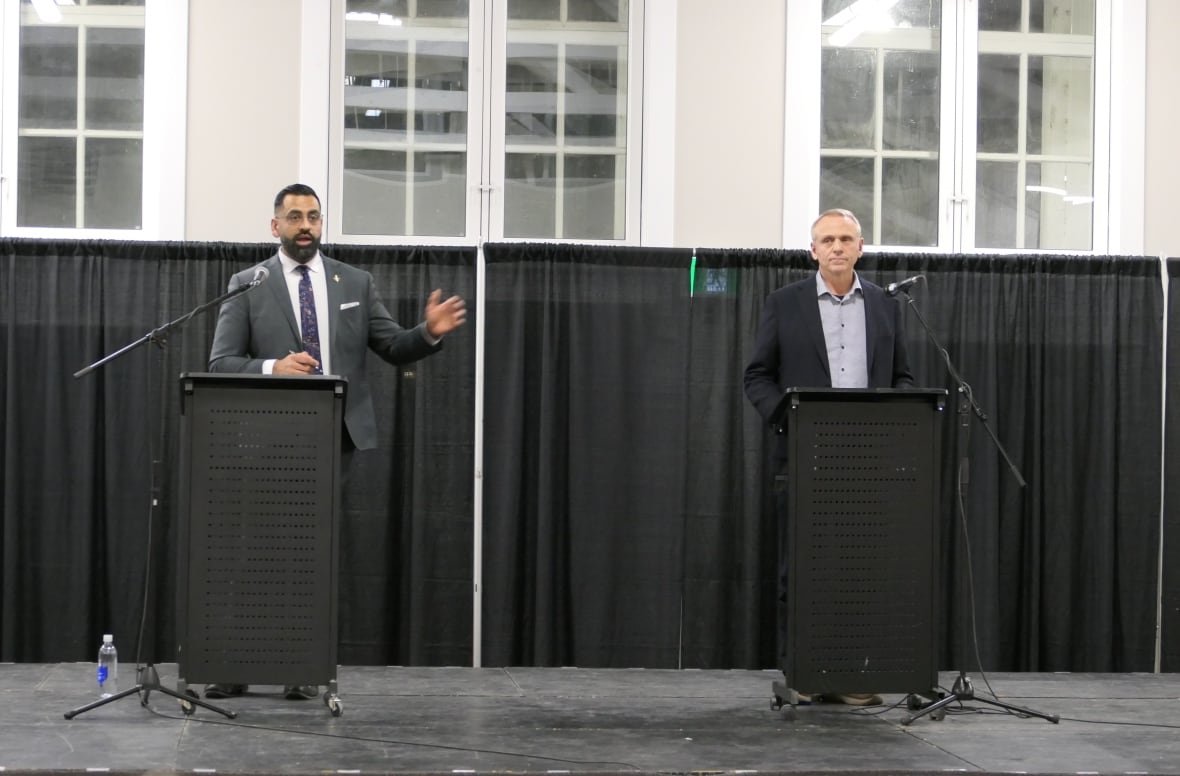 obby-khan-wally-daudrich Two men stands behind two podiums on a stage, with a black backdrop behind them.