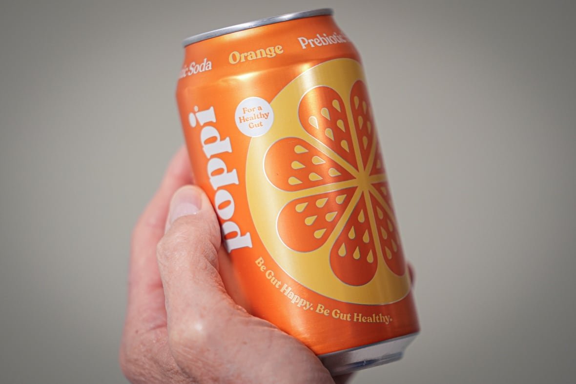 A person holds an orange can of soda.