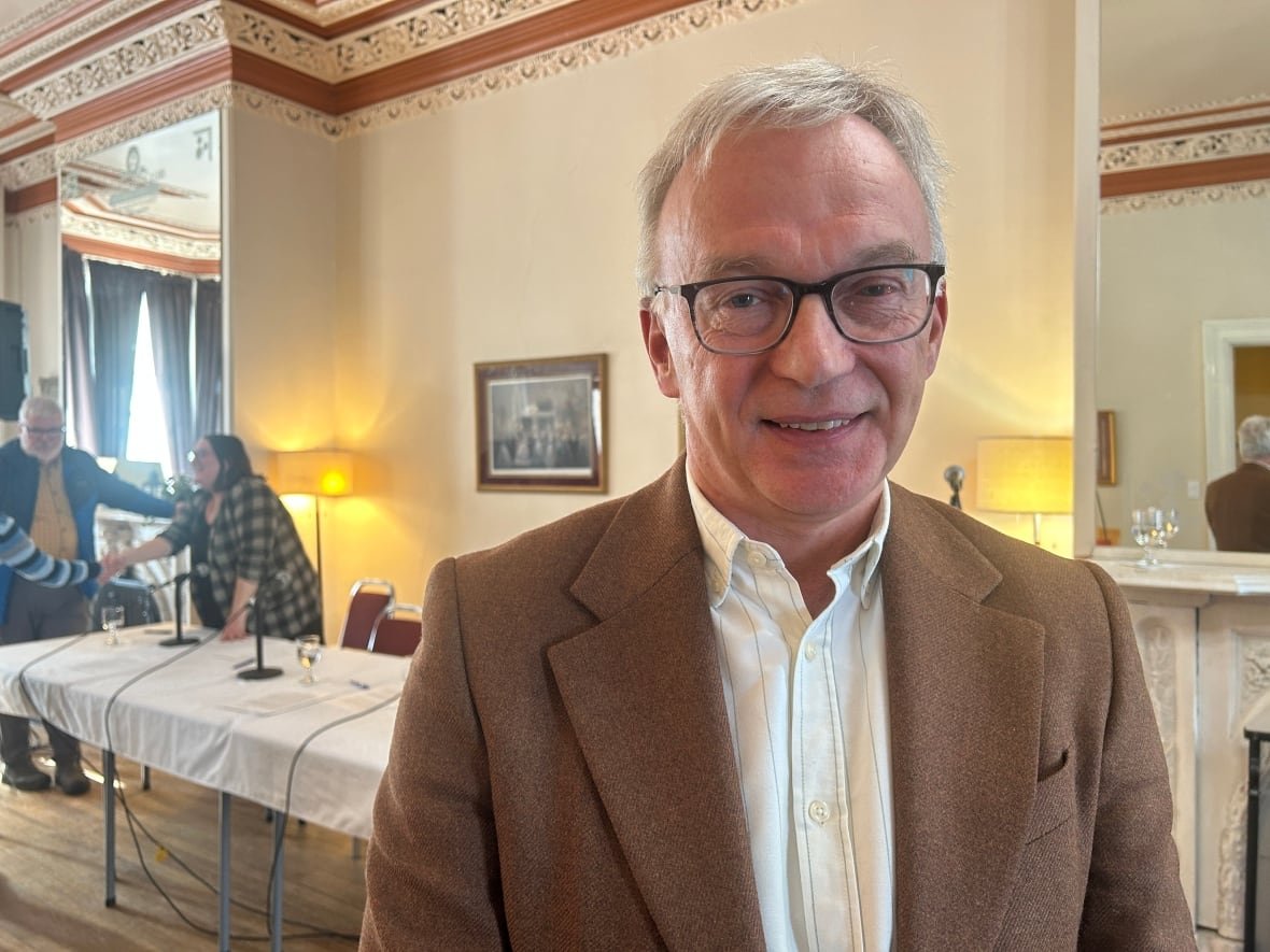 sean-casey A man in a brown blazer smiling in a decorated room with a table and people in the background