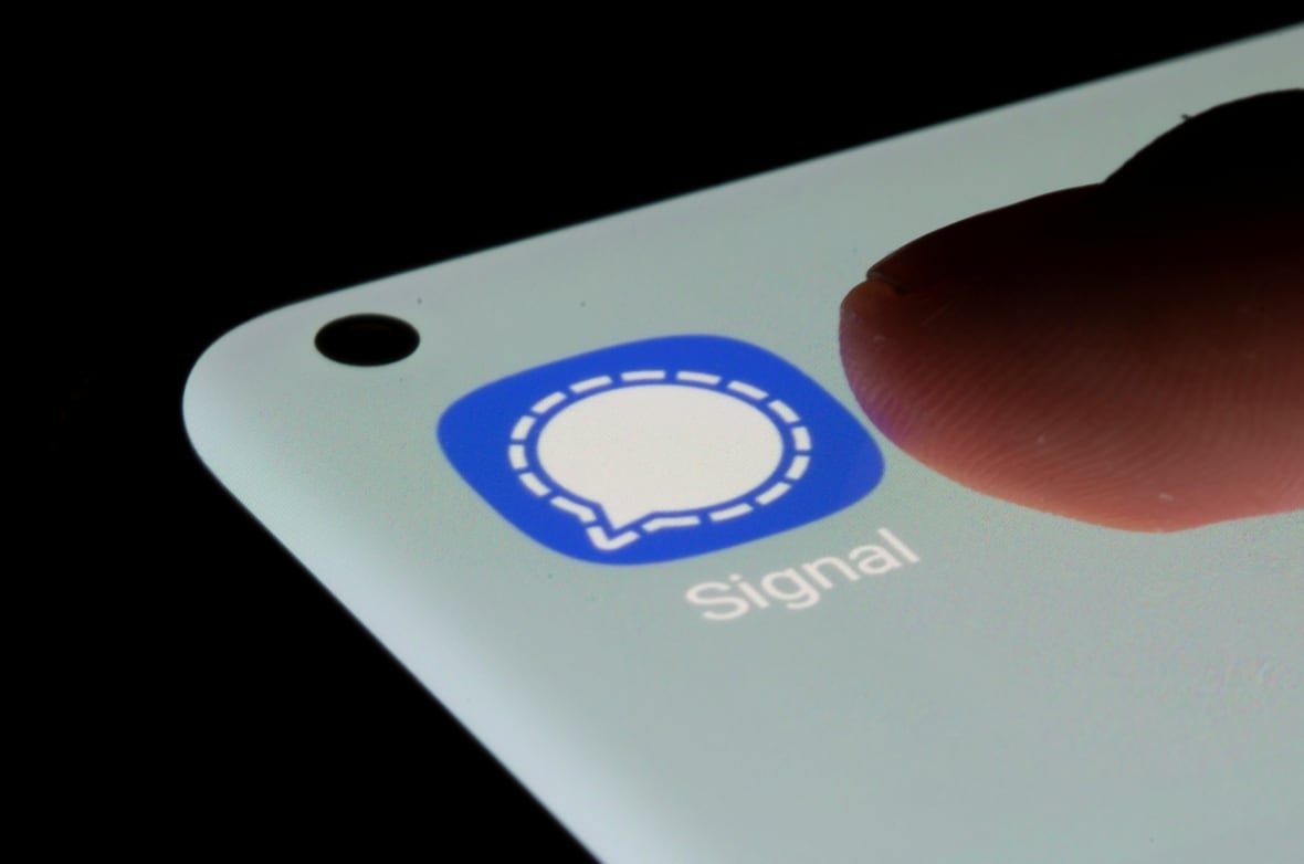 tech-signal A finger hovers over a smartphone showing the blue icon for the Signal messaging app