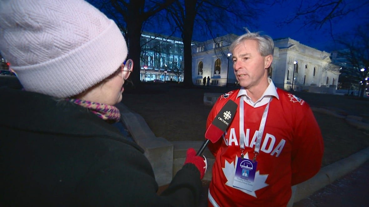 tim-houston-canada-jersey A man wearing a Canada hockey jersey speaks into a microphone.