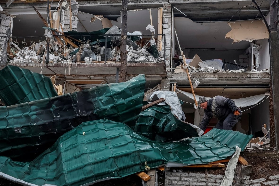 Man steps over what remains of his roof as he clears rubble left by a Russian drone strike.