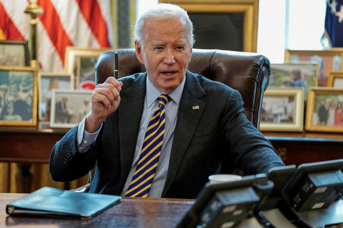 usa-biden A person holds up a pen while sitting and talking at a table.