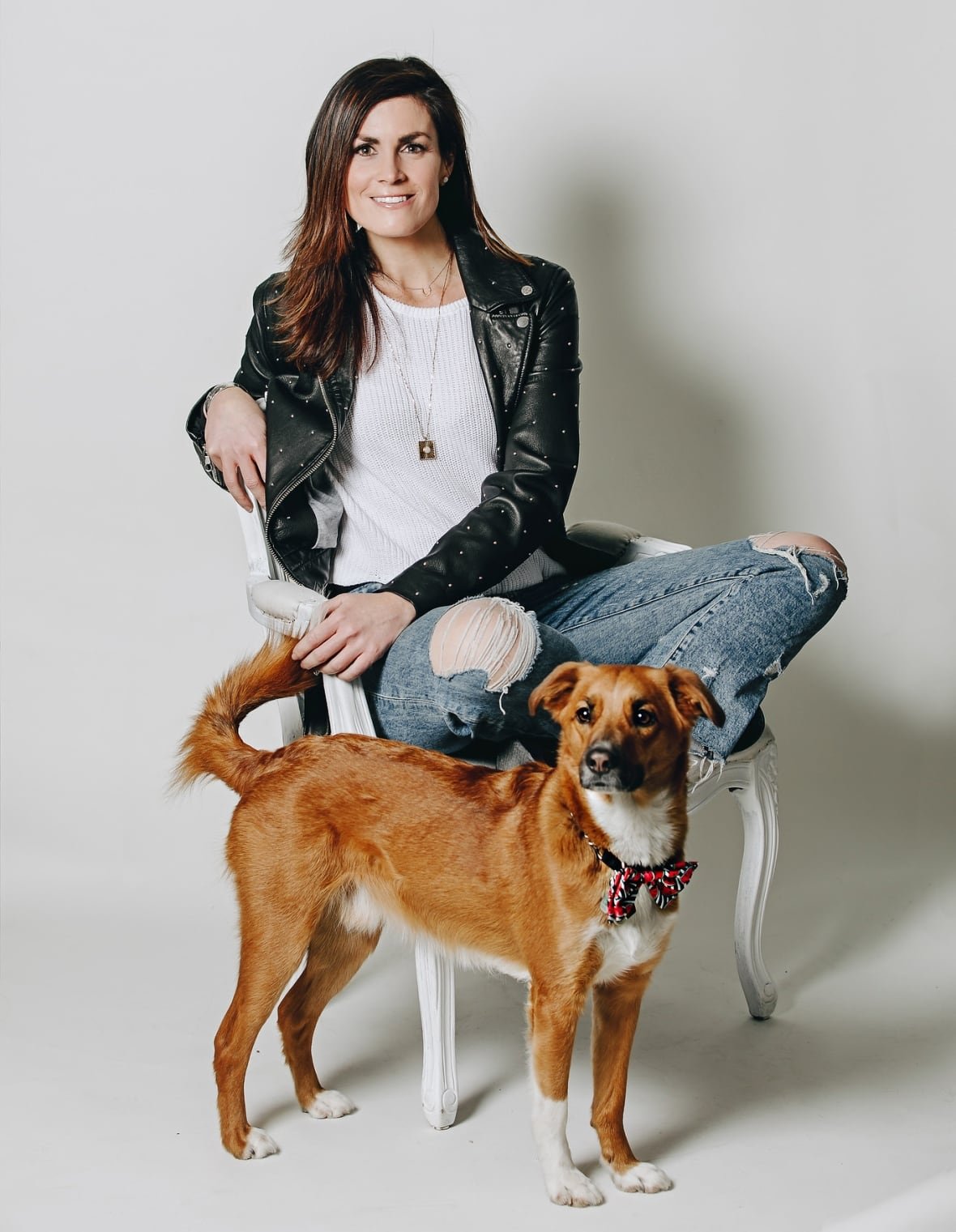 whitney-titheridge-jpeg A woman standing in a chair, with a medium-sized brown dog standing in front of her.