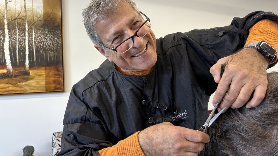 zuheir-bechara-1 A man smiles as he trims a client's hair with a pair of scissors.