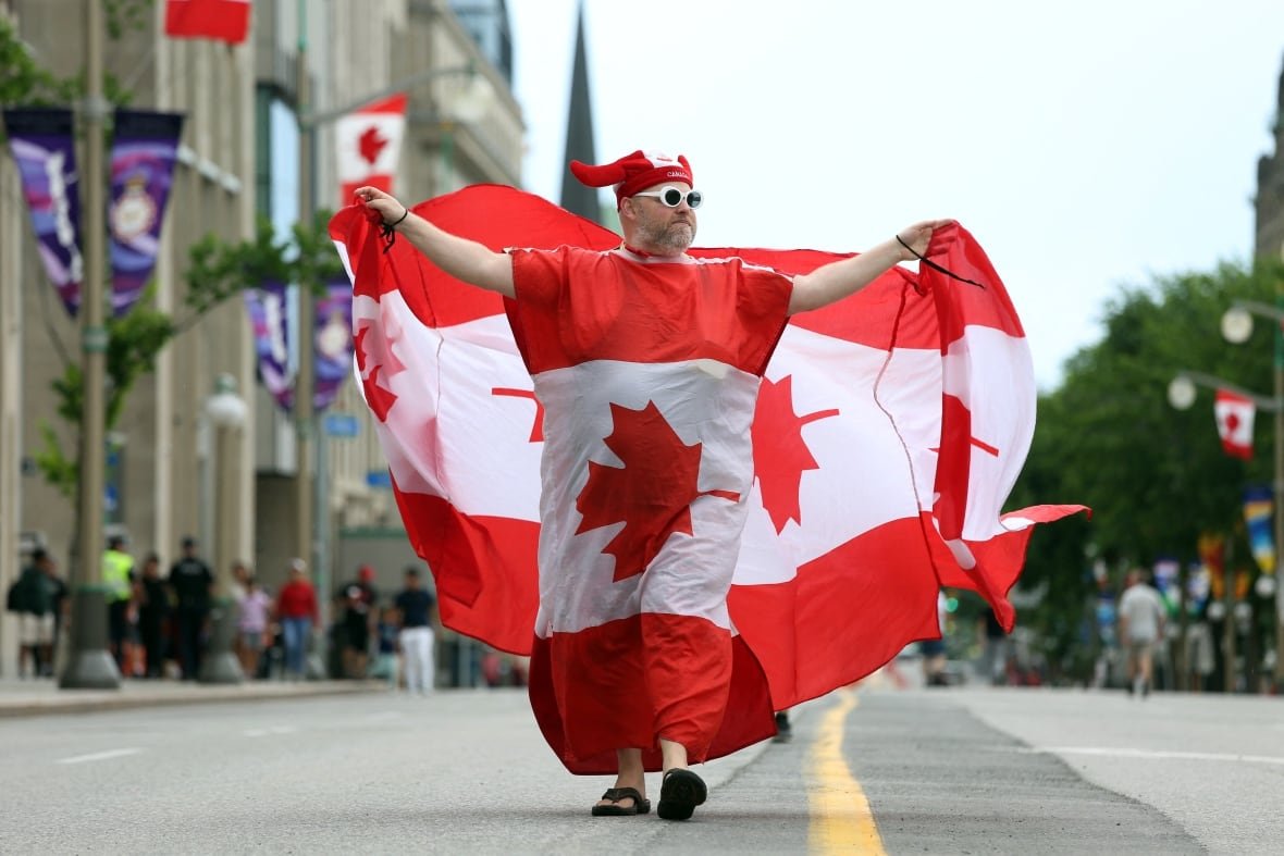 1241650607 A person draped in a Canadian flag walks down a street.