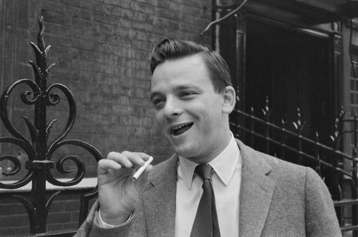 2183522734 Black and white phot of a smiling man in a suit holding a cigarette