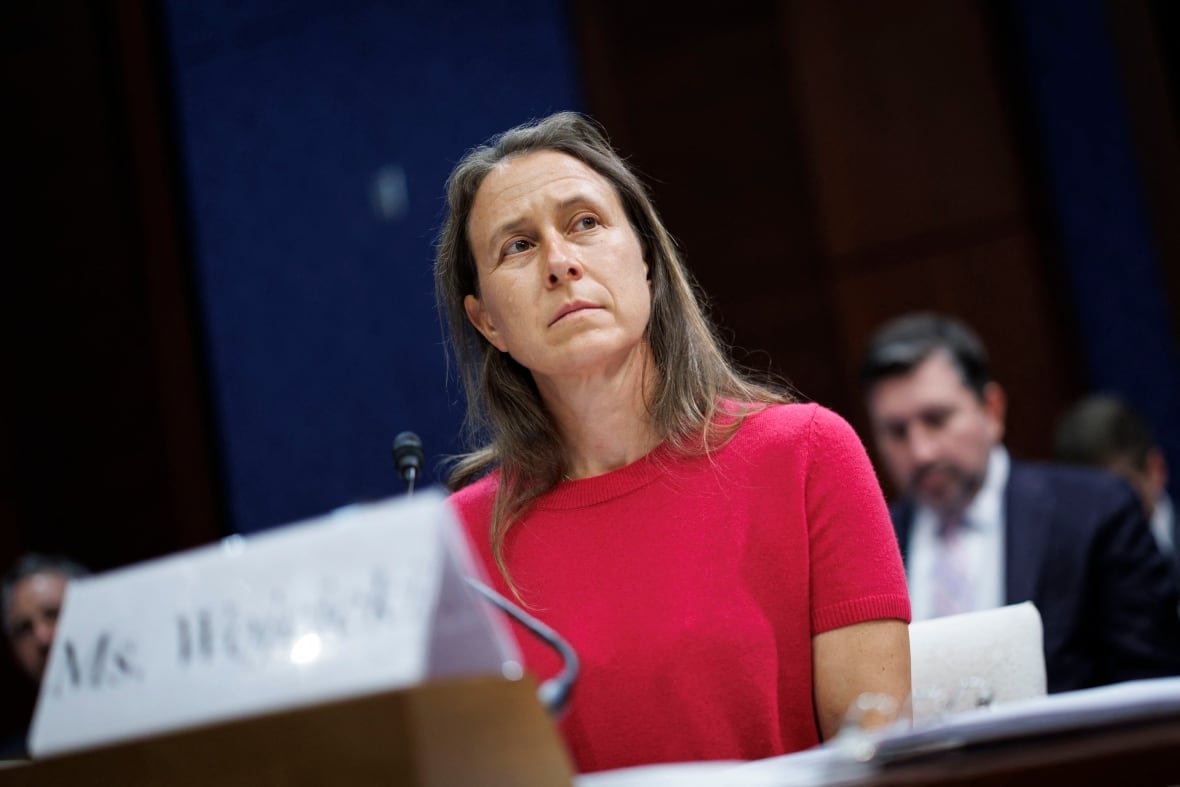 2218937083-23andme-anne-wojcicki A woman with long graying hair sits in front of a microphone and peers to one side.
