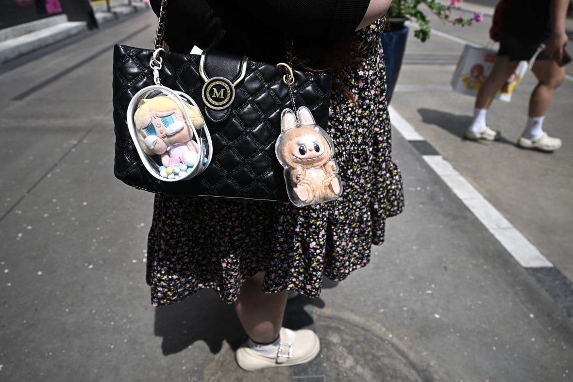 Two figurines are attached to a designer handbag.