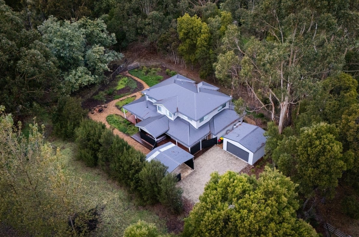 2222981338 An aerial view of a home that appears to be in rural area, surrounded by trees, is shown.