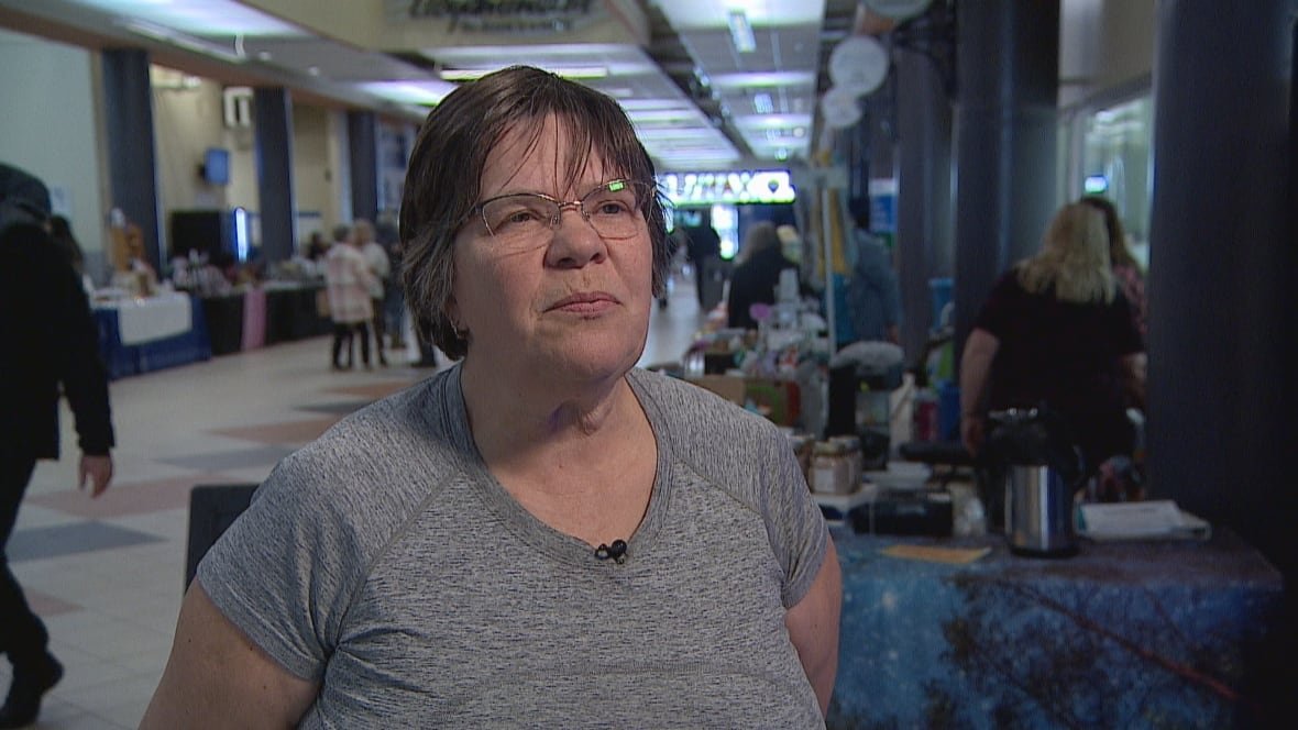 alice-pattison A woman wearing glasses and a grey t-shirt stands among food vendors.