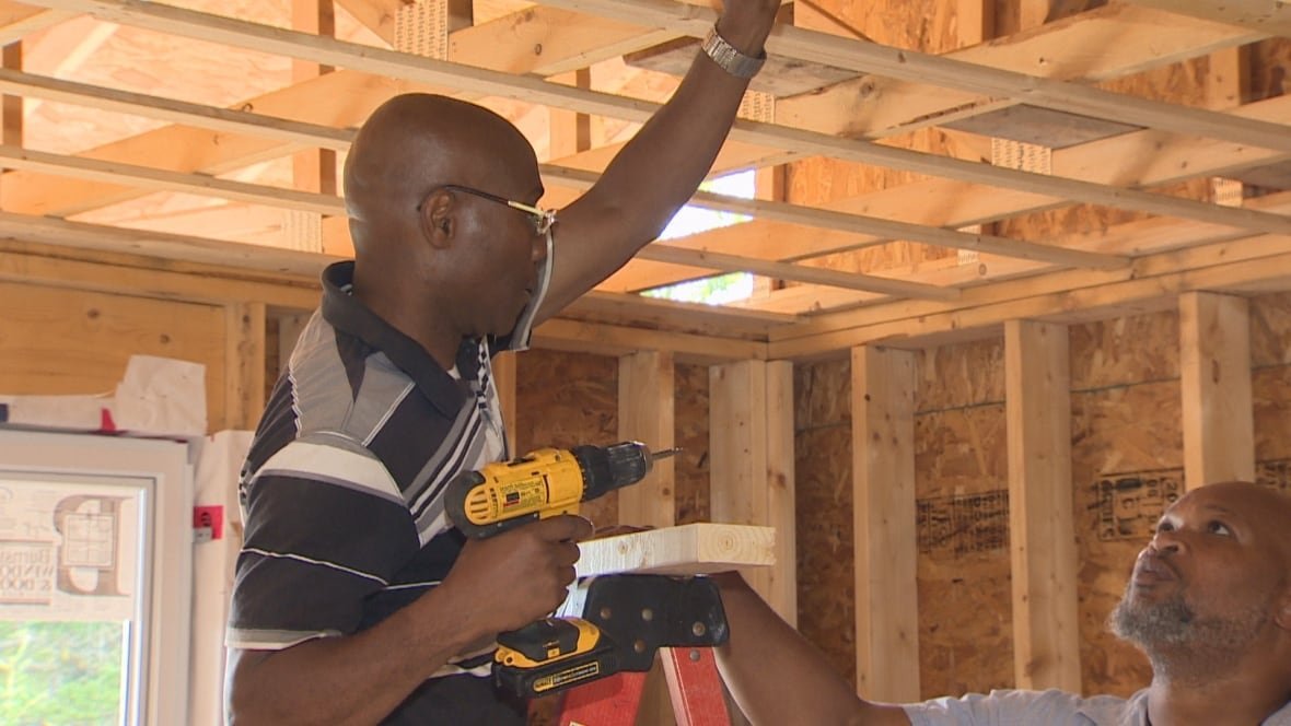 apprentice-vincent-kennedy-learns-on-the-job-from-howard-benjamin A Black man holding a drill working working on a house frame