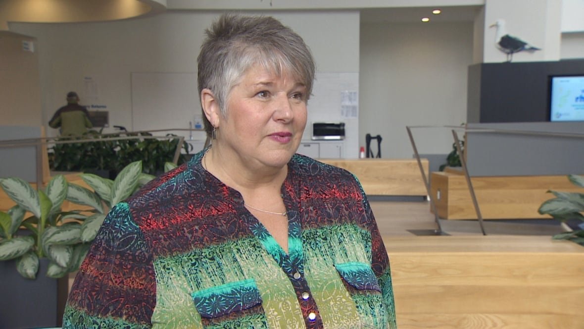 becky-kent-halifax A white woman with short grey hair stands in the vestibule of a library with plants visible behind her