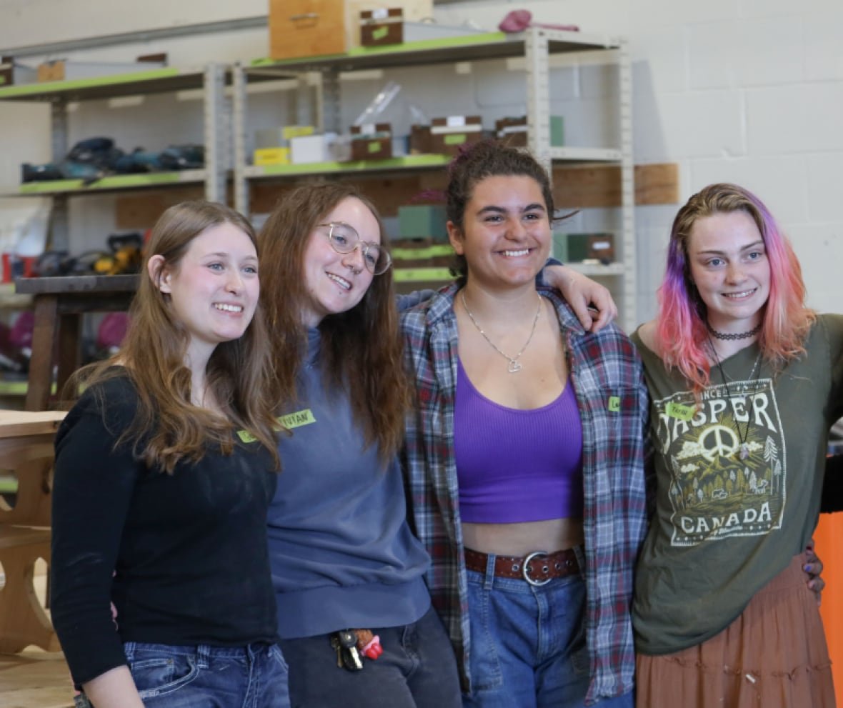calgary-shop-class Four young women link arms for a photo in a woodworking shop.