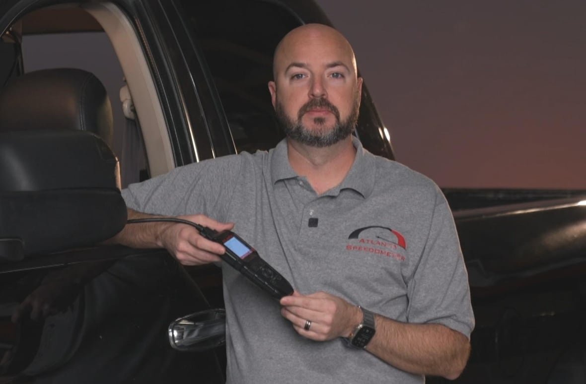 carfax Man leaning on black truck, holding odometer programming device.