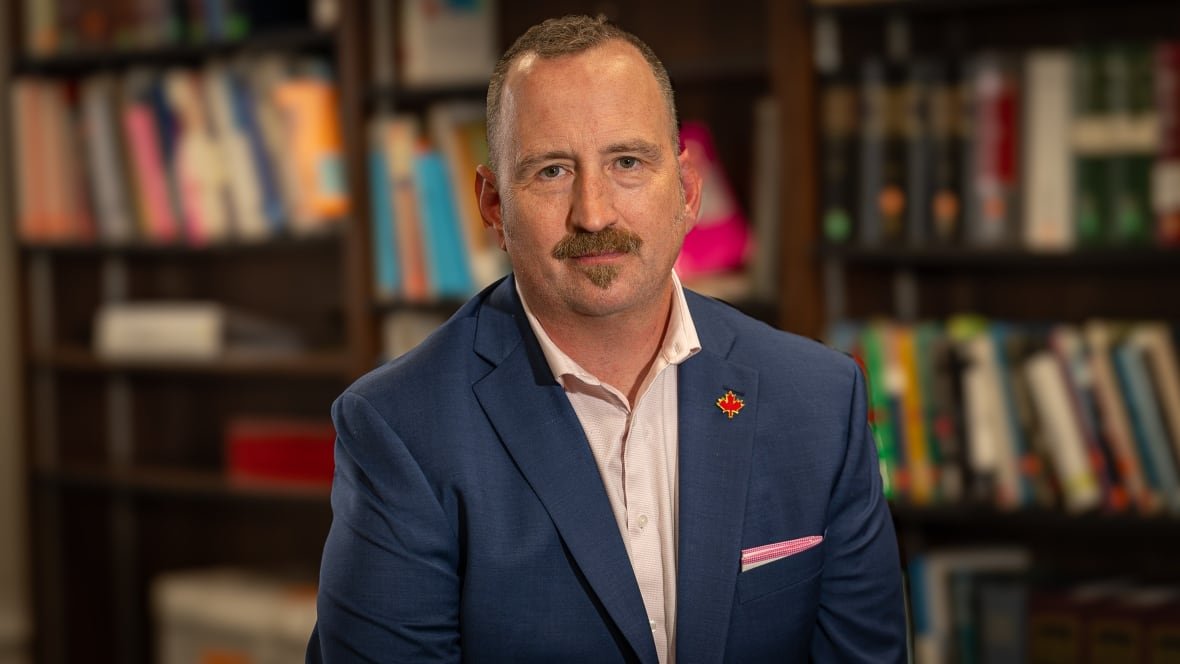 geoff-white Headshot of man in suit with books in the background.