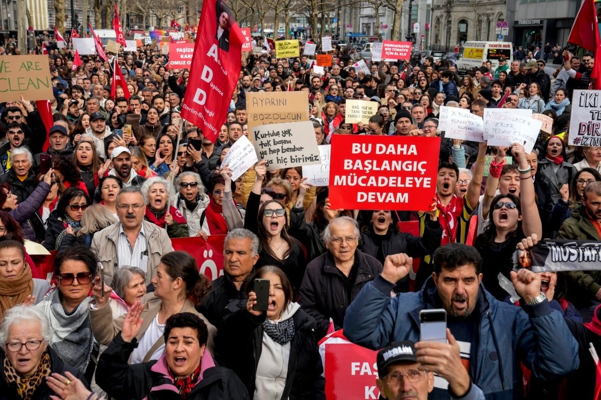 germany-turkey-politics People in a crowd of protesters hold signs.