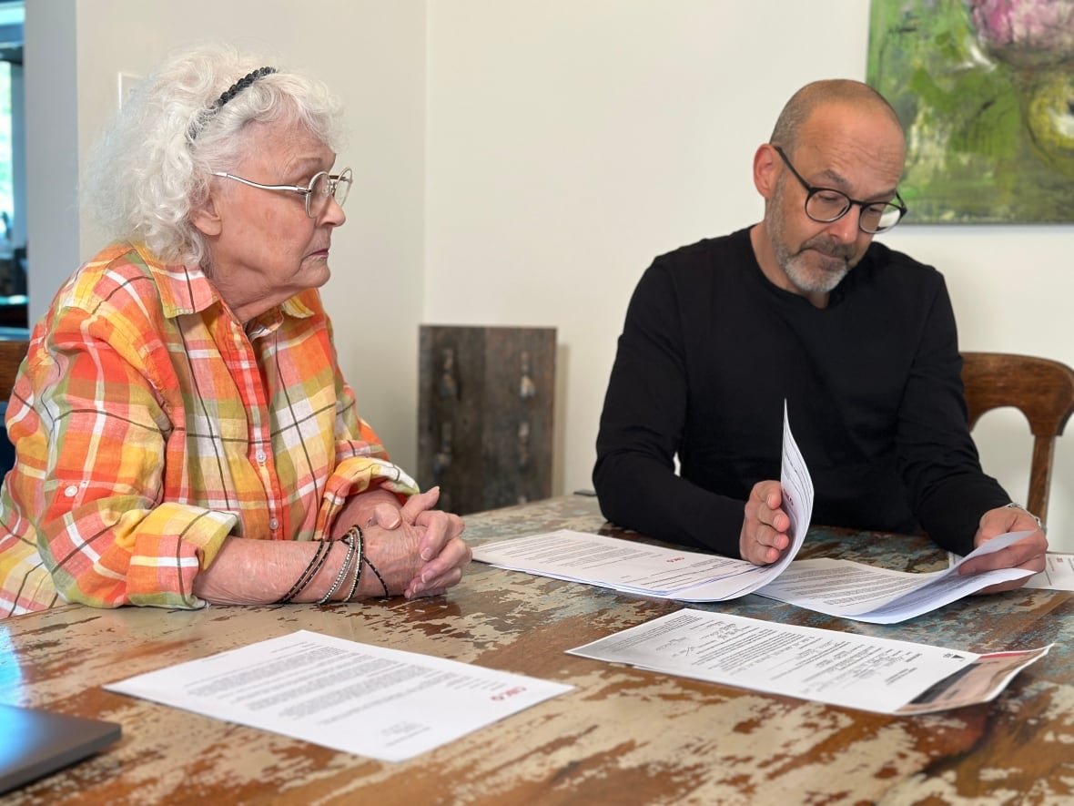 go-public-cibc-paperwork An older woman with curly white hair and glasses sits at a dining room table next to a balding middle-aged man with glasses as he flips through several pieces of paperwork.